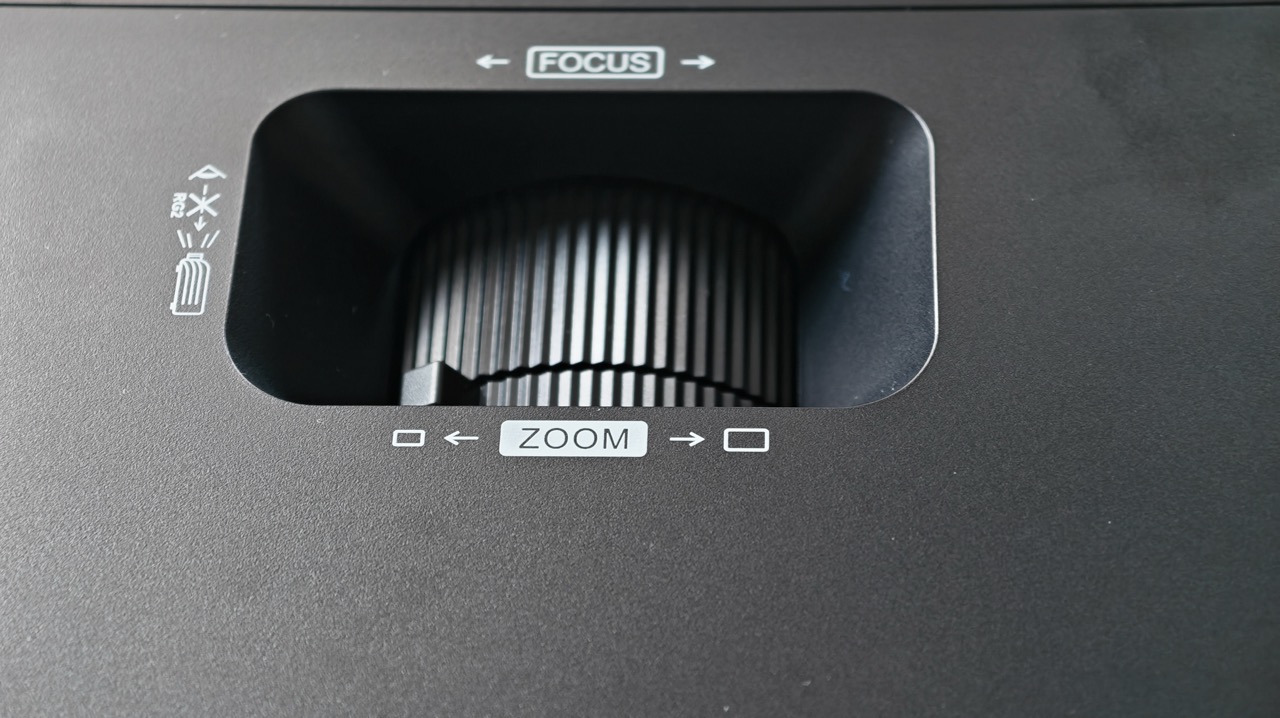 ViewSonic LX720-4K RGB tesztA 2000 ANSI lumen és a 3 000 000:1 dinamikus kontrasztarány sötétített szobában egyenesen lenyűgöző képet eredményez. Teljesen sötétített szobában a kép mélysége és a feketék minősége vetekszik azzal, amit egy prémium OLED tévén megszokhatunk – természetesen nem DLP technológia esetén abszolút fekete nem lehetséges, de a projektor ezzel az értékkel a kategória legjobbjai között van. ViewSonic Nappalifénynél azonban a 2000 lumen némi engedményt kér. Teljesen megvilágított szobában halvány lesz a kép, elsötétítéssel viszont már elfogadható, és teljes sötétítéssel egyenesen lenyűgöző. Ez nem gyengeség, hanem a kategória természetes korlátja – aki főleg nappal, sok beeső fénnyel szeretne vetíteni, annak érdemes a magasabb lumentartományba eső modelleket is megvizsgálni. Telepítési rugalmasság Az 1,3-szoros optikai zoom, az oldalirányú vetítés, a vízszintes és függőleges trapézkorrekció, valamint a négypontos és torzításkorrekció szinte bármilyen szobai elrendezést lehetővé tesznek. A tesztidőszak alatt a projektort három különböző pozícióból is kipróbáltuk – dohányzóasztalról, mennyezeti tartóról és oldalról, szögből vetítve –, és minden esetben percek alatt tökéletes képet adott a korrekciós rendszer. ViewSonic A fókusz manuális, ami az egyetlen pont, ahol hiányzott az automatikus megoldás. Mozgatás után mindig kézzel kell visszaállítani a fókuszt – rutinná válik, de az első néhány alkalommal felesleges extra lépésnek tűnik. Gaming – komolyan veendő Az 1 ms-os input lag és a VRR támogatás biztosítja, hogy gyors tempójú játékoknál is folyamatos és pontos legyen a kép. Néhány órán át játszottunk akciójátékokkal és versenyautós szimulátorral – a késleltetés egyáltalán nem volt érzékelhető, és a képfrissítés folyamatos volt. Aki nagy képméreten szeretne játszani input lag nélkül, annak az LX720-4K RGB valódi alternatíva a hatalmas tévékkel szemben. ViewSonic Hang – a projektor gyenge pontja A beépített hangszóró alapvetően elvégzi a feladatát, de nem több annál. Filmnézéshez különálló hangrendszer vagy soundbar erősen ajánlott. Ez nem meglepő egy ilyen kategóriájú projektorban – a gyártó nyilván a képre koncentrált, és helyesen tette –, de érdemes tudni, hogy az LX720-4K RGB vételárán felül érdemes hangrendszerre is tervezni. Google TV – streaming egyből A beépített Google TV az egyik legnagyobb kényelmi előny. Netflix, Disney+, YouTube, Prime Video – mind azonnal elérhető, bejelentkezés után azonnal készen áll a vetítés. Az alkalmazásbolt széleskörű, a felhasználói felület gyors és logikus. Airplay és Miracast is támogatott, így iPhone-ról és Android eszközről egyaránt tükrözhető a tartalom. Fényforrás és hosszú távú működés A lézer fényforrás normál üzemmódban 20 000, öko módban 30 000 óra élettartamot ígér – lámpacsere szükségessége nélkül. Ez azt jelenti, hogy ha naponta három órát vetítünk, több mint 18 évig tarthat a fényforrás – a lámpa életkori aggodalom egyszerűen nem létezik ezzel a készülékkel. LDLC Összességében – a legjobb szín, amit projektorban látni Az LX720-4K RGB egyetlen területen kiemelkedik az összes vetélytársa fölé: a színek terén verhetetlen ebben az árkategóriában. Az RGB háromszínű lézer olyan képet ad, amelyre első pillantásra megáll az ember – a BT.2020 teljes lefedettsége nem elméleti adat, hanem valóban látható különbség a mindennapi tartalmakon. A gaming teljesítmény, a rugalmas telepítési lehetőségek és a beépített Google TV tovább erősítik a képet. Aki sötétített szobában, kizárólag képminőségre fókuszálva keres projektort, és hajlandó külön hangrendszerbe is befektetni, annak az LX720-4K RGB az egyik legjobb döntés a piacon. Aki nappalban, sok beeső fénnyel szeretne vetíteni, vagy Dolby Vision tartalmakat kizárólag azzal a szabvánnyal szeretne nézni, annak érdemes tovább körülnézni.